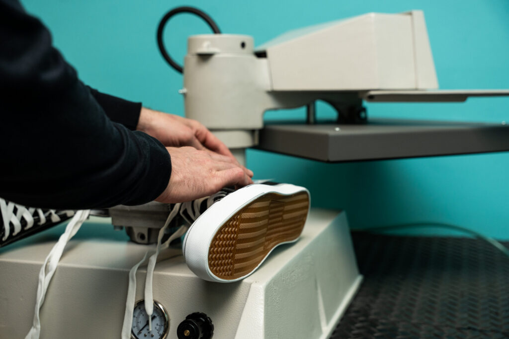 Heat press machine applying heat transfer to sneaker sole, showcasing precision industrial apparel decoration equipment by Insta Graphic Systems