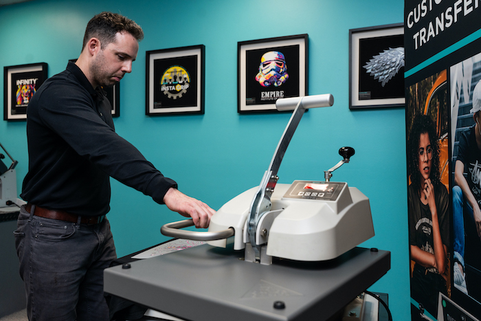 Insta Graphic Systems team member operating an Insta heat press machine in a custom apparel production showroom.
